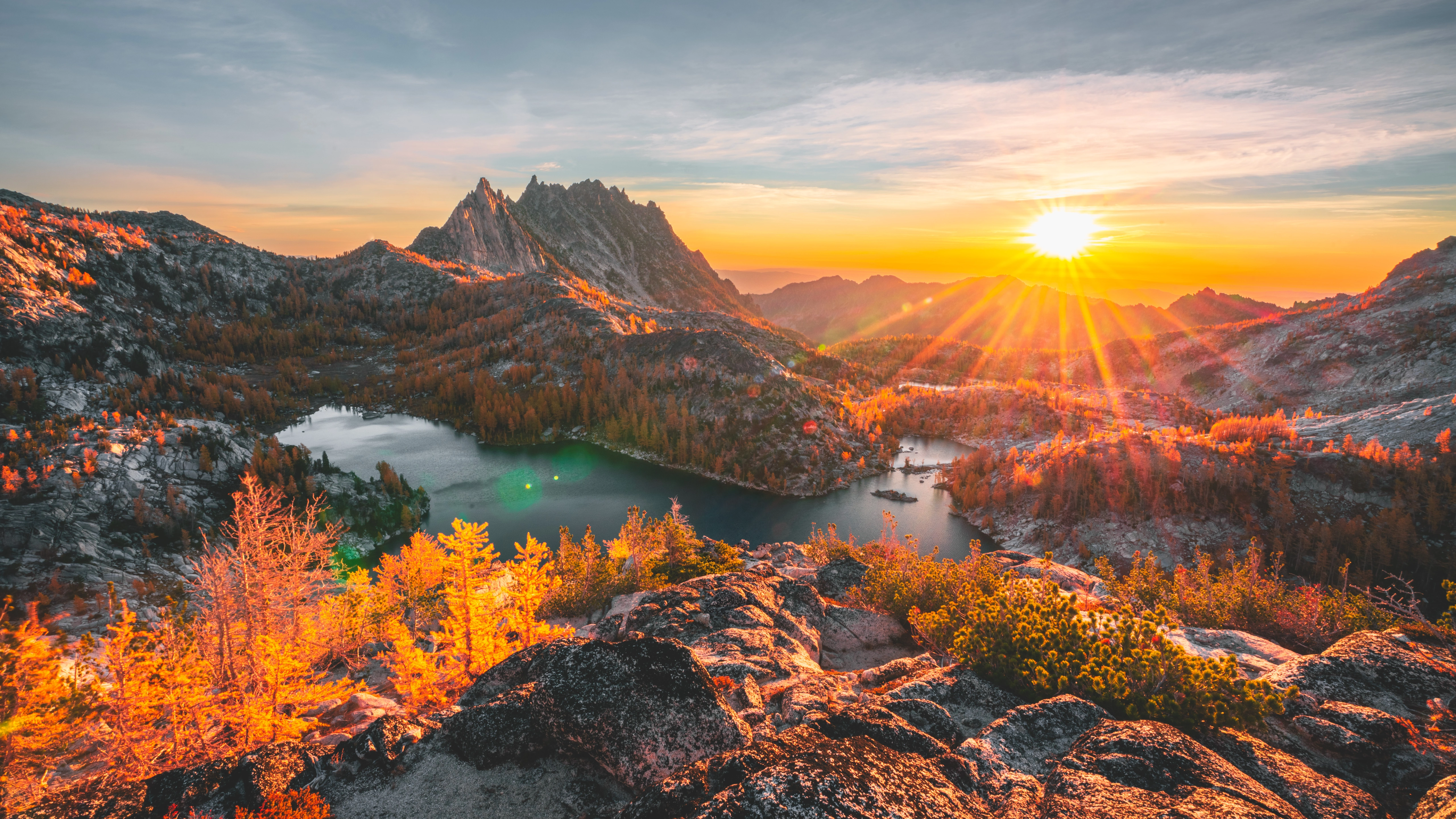 Sunrise over an alpine lake, jagged mountains and golden autumn trees.