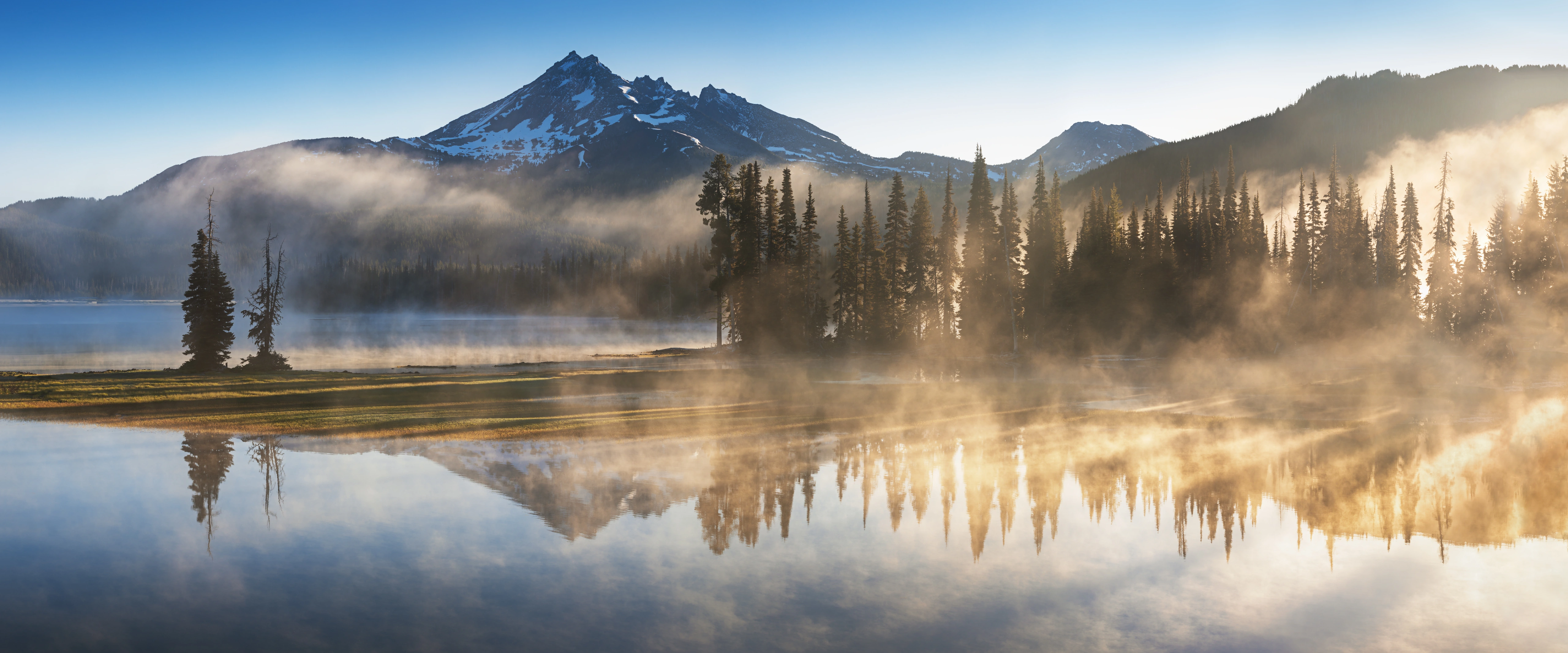 Morning light and mist over a mountain lake and pine forest.
