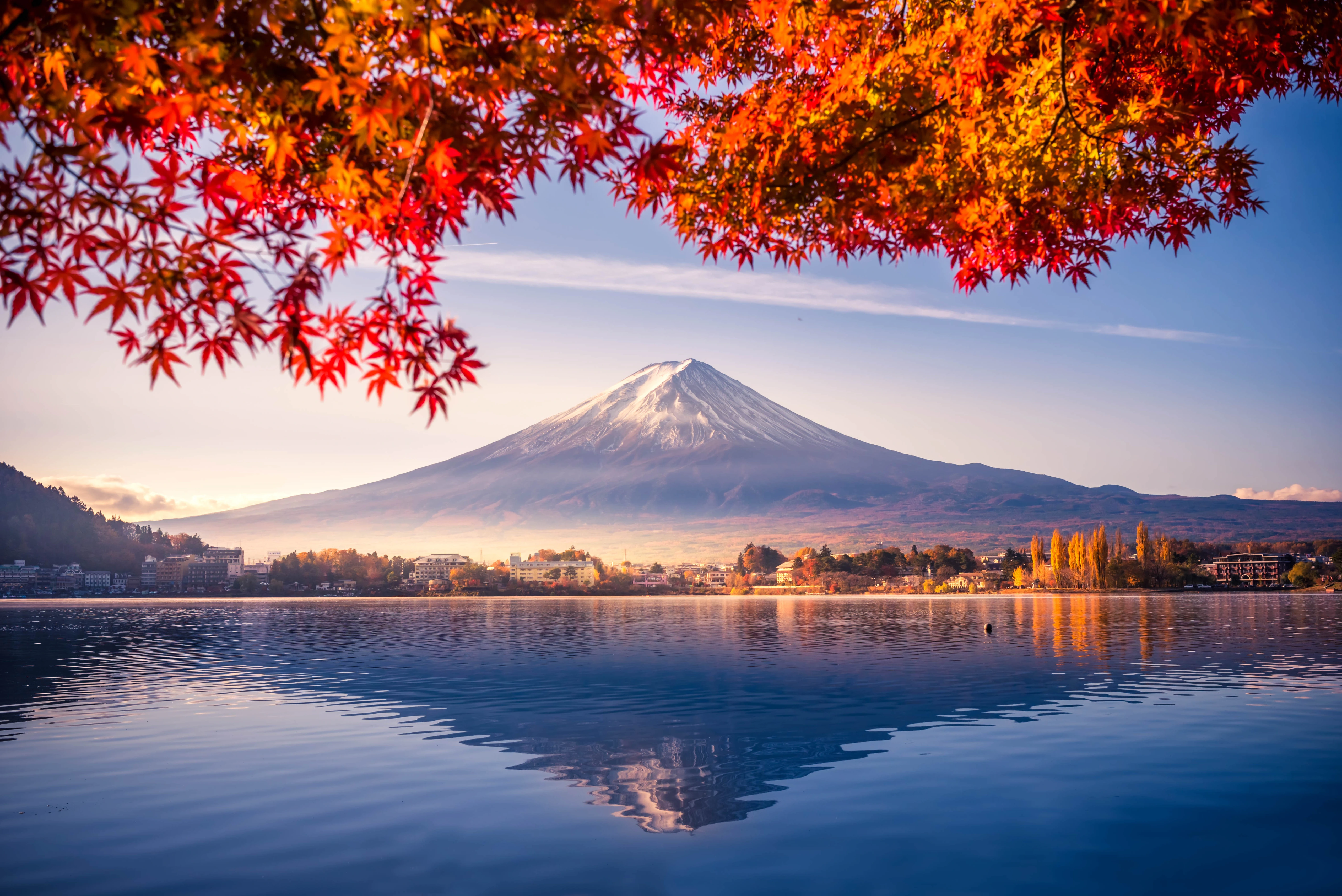 Mount Fuji reflected in a still lake, framed by red and gold autumn leaves.